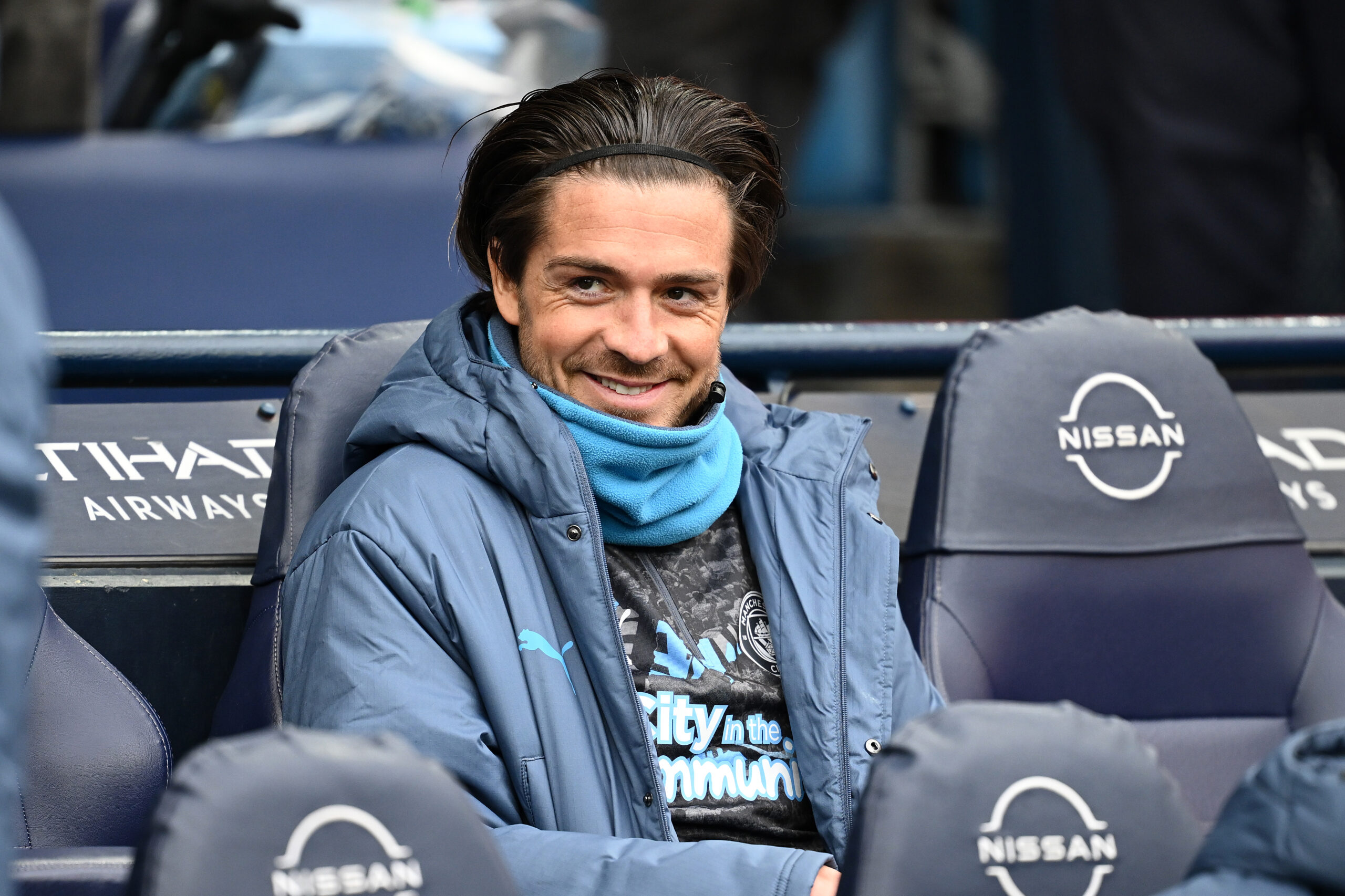 Jack Grealish sitting on the Manchester City bench during a 2025 Premier League match, looking pensive as speculation over his future grows.